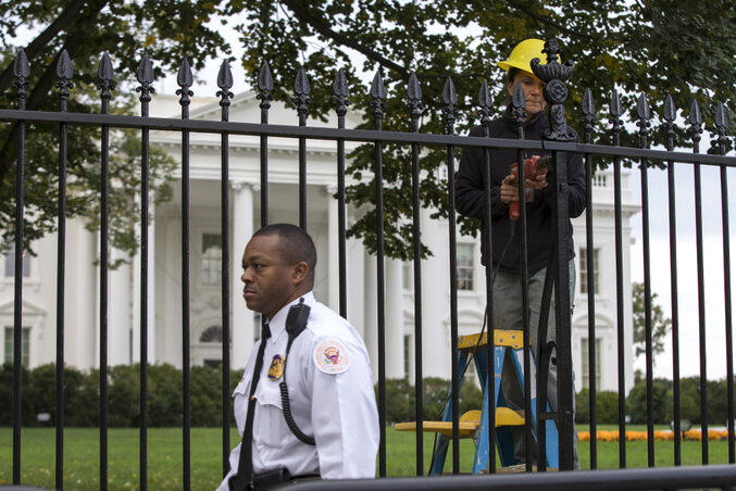 A biztonsági szolgálat (Secret Service) embere járőröz, míg egy munkás javítja azt a helyet, ahol a marylandi fiatal átmászott a kerítésen (Fotó: Beta/AP)