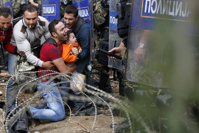 Egy, a rohamrendőrök és a tömeg közé szorult migráns a gyermekével Idomeniben, a görög–macedón vasúti határátkelőnél kitört incidens során (Fotó: Beta/AP)