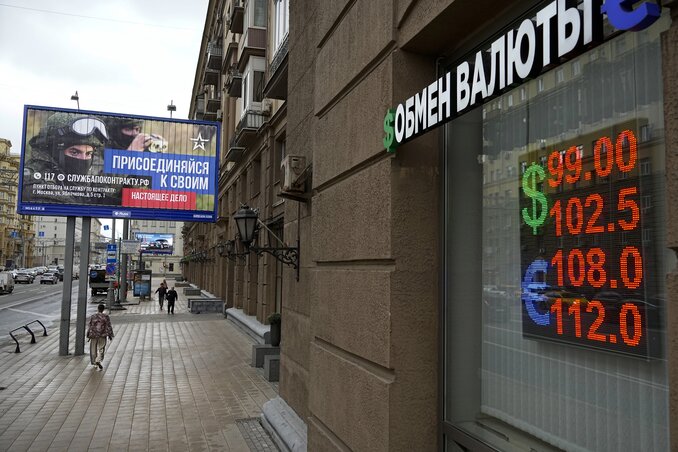 People walk past a currency exchange office with an army recruiting billboard calling for a contract for service in the Russian armed forces in Moscow, Russia, Monday, Aug. 14, 2023. The Rus